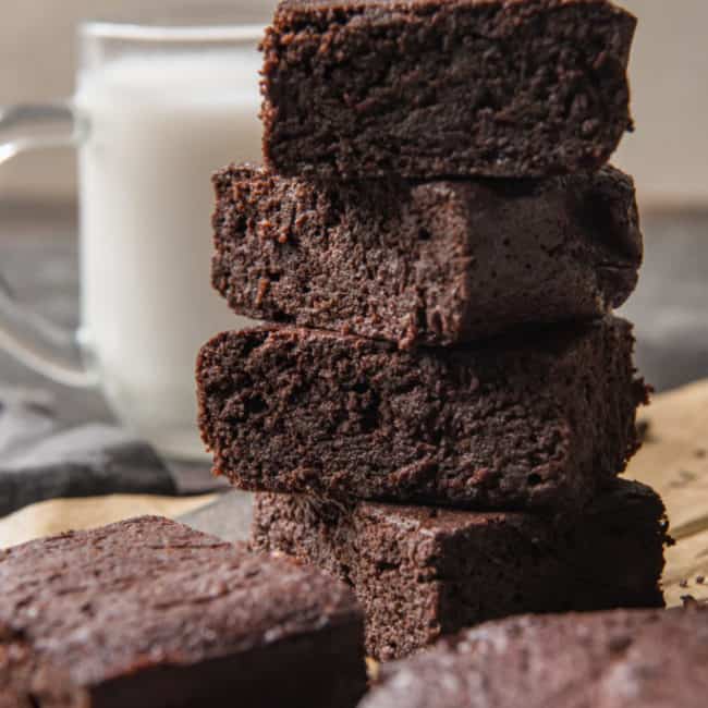 keto brownies stacked with other brownies in the foreground and a glass of milk nearby